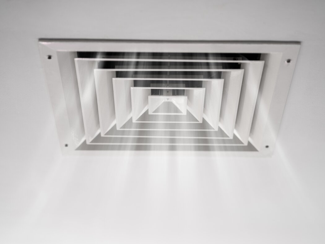 Deckenlüftungs-Modul einer zentralen Klimaanlage. Zu sehen ist ein weißes Gitter, aus dem Luft herausströmt.