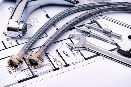 Eine Sanitärarmatur, ein Schraubschlüssel und Schläuche liegen auf einem Bauplan für die Badplanung.